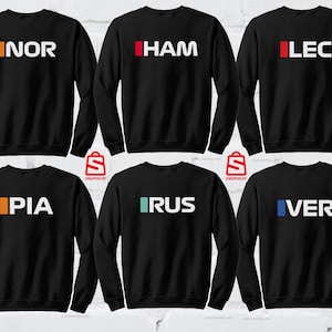 Puede incluir: Seis sudaderas negras con texto blanco y barras de colores. Cada sudadera muestra un nombre diferente de tres letras: NOR, HAM, LEC, PIA, RUS y VER. Las sudaderas son probablemente para un equipo deportivo o ropa de aficionado.