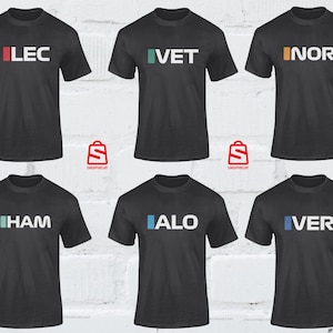 Puede incluir: Seis camisetas negras con cuadrados de diferentes colores y nombres impresos en la parte delantera. Los nombres son LEC, VET, NOR, HAM, ALO y VER.