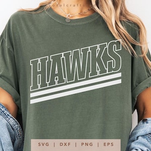 May include: Olive green t-shirt with the word "HAWKS" in white, outlined in green, and two white horizontal stripes. The shirt has rolled-up sleeves and is made of a soft material. The bottom of the shirt has the text "SVG | DXF | PNG | EPS".