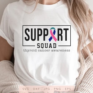 May include: White t-shirt with the words "SUPPORT SQUAD" in a black box, with a teal, pink, and blue ribbon graphic. Below the box, the text reads "thyroid cancer awareness". The shirt is a casual style.