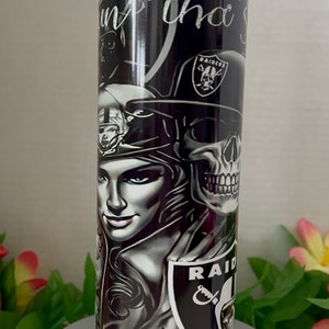 Könnte beinhalten: Ein schwarz-weißer Becher mit einem Totenkopf und einem Frauenkopf. Der Becher ist mit den Worten "RAIDERS" und "Baby Girl" verziert.