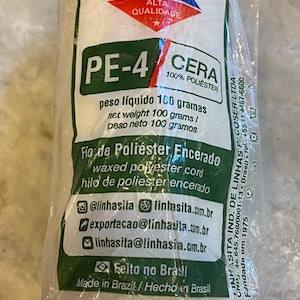 May include: A spool of white Linhasita PE-4 waxed polyester cord wrapped in clear plastic packaging. The label displays the brand name, 100 grams net weight, and contact information. The cord is made in Brazil and is 100% polyester material.