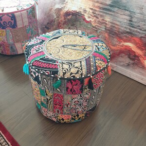 May include: A round, multi-colored, patchwork ottoman with tassels. The ottoman is made of fabric with a variety of patterns and colors, including black, red, pink, blue, and green.