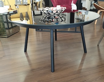 May include: A round black coffee table with a reflective glass top and black metal legs. A decorative bowl with a silver rim and mirrored accents sits on the table. The table is approximately 36 inches in diameter.