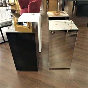 May include: Three modern accent tables. One is black, one is white, and the third has a mirrored finish. The tables are rectangular and stand on a wooden floor. The tables are in a showroom setting.