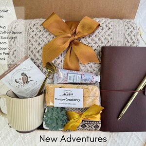 May include: A gift box filled with various items, including a throw blanket, a journal, a coffee mug, a succulent, and a handwritten note that says "New Adventures".