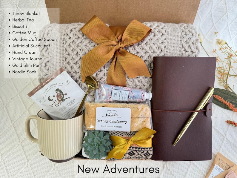 May include: A gift box filled with various items, including a throw blanket, a journal, a coffee mug, a succulent, and a handwritten note that says "New Adventures".
