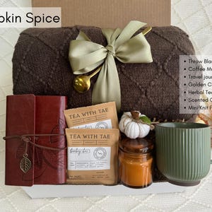 K&ouml;nnte beinhalten: Ein Geschenkset mit einer braunen Decke, einer gr&uuml;nen Kaffeetasse, einem Reisetagebuch und Kr&auml;utertee. Das Set enth&auml;lt einen goldenen Kaffeel&ouml;ffel, eine Duftkerze und einen Mini-Strickk&uuml;rbis. Der Text "Pumpkin Spice" ist sichtbar.