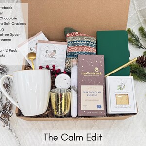 Puede incluir: Una caja de regalo llena de art&iacute;culos de cuidado personal. Incluye una taza de caf&eacute; blanca, chocolate negro, un cuaderno verde, un bol&iacute;grafo dorado, galletas saladas, t&eacute;, sales de ba&ntilde;o, una vela y calcetines estampados. La caja est&aacute; etiquetada como "The Calm Edit".