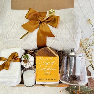 Peut inclure: Un panier-cadeau rempli d'articles confortables, dont une couverture blanche, une serviette blanche, une bougie blanche, une petite citrouille blanche, une th&eacute;i&egrave;re en verre avec un infuseur en acier inoxydable et une bo&icirc;te de th&eacute; aux herbes &eacute;tiquet&eacute;e "Cup of Sunshine" par Big Heart Teas.