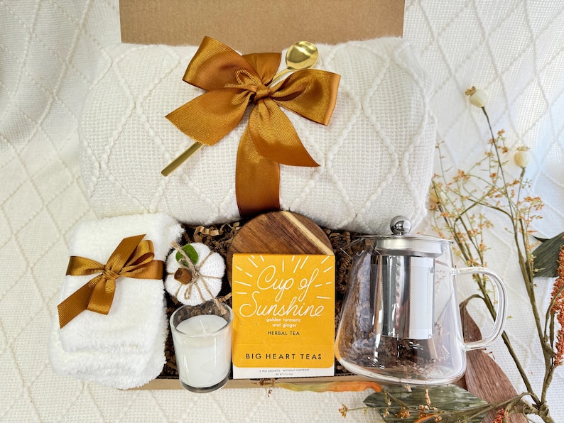 Peut inclure: Un panier-cadeau rempli d'articles confortables, dont une couverture blanche, une serviette blanche, une bougie blanche, une petite citrouille blanche, une th&eacute;i&egrave;re en verre avec un infuseur en acier inoxydable et une bo&icirc;te de th&eacute; aux herbes &eacute;tiquet&eacute;e "Cup of Sunshine" par Big Heart Teas.
