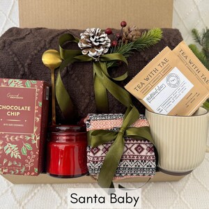 May include: A gift basket with a brown knitted blanket, a red candle, a box of chocolate chip cookies, a mug, and two packages of tea labeled "Tea with Tae".