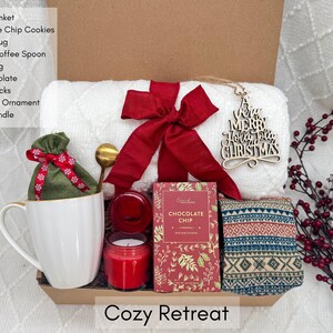 Puede incluir: Una caja de regalo "Cozy Retreat" contiene una manta blanca, galletas con chispas de chocolate, una taza de caf&eacute;, una cuchara dorada, una bolsa de arpillera, chocolate caliente, calcetines n&oacute;rdicos, un adorno navide&ntilde;o y una vela perfumada.