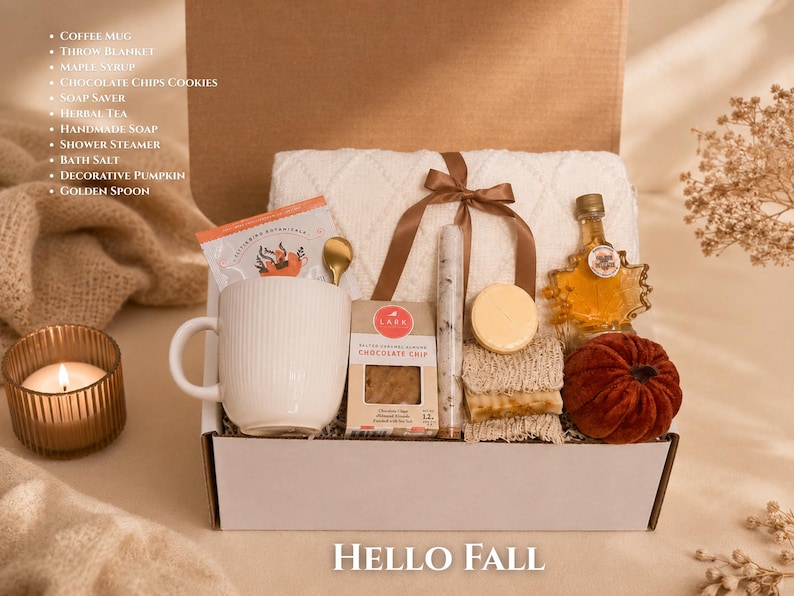 May include: A gift box containing a white ribbed mug, a cream throw blanket with a brown ribbon, a bottle of maple syrup, chocolate chip cookies, a soap saver, herbal tea, handmade soap, a shower steamer, bath salt, a pumpkin, and a golden spoon.