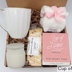 May include: A gift box filled with a white mug, a candle, a package of orange cranberry biscotti, a white hand towel with a pink ribbon, and a pink box of "Cup of Love" herbal tea.