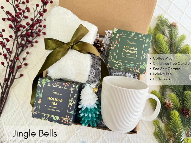Puede incluir: Una caja de regalo con una taza blanca, una toalla blanca atada con una cinta verde y dos cajas de golosinas. Tambi&eacute;n se incluye una vela de &aacute;rbol de Navidad verde y blanca y bayas rojas. El texto "Jingle Bells" est&aacute; en la parte inferior.