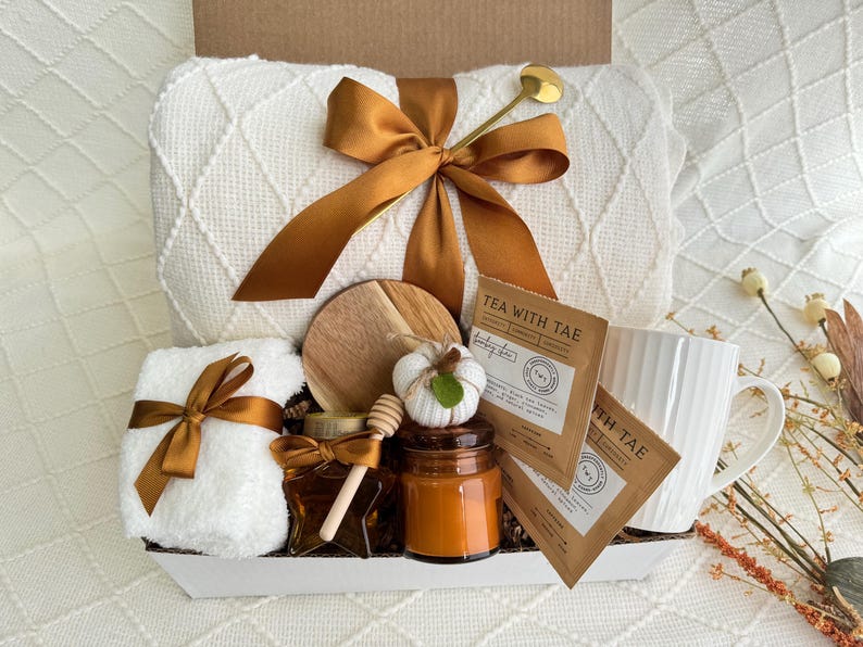Peut inclure: Un panier-cadeau blanc rempli d'articles confortables pour une soir&eacute;e relaxante. Il comprend une couverture blanche, une serviette blanche, une tasse, une bougie, un pot de miel, un sous-verre en bois et deux sachets de th&eacute;. Les sachets de th&eacute; sont &eacute;tiquet&eacute;s "Tea with Tae".