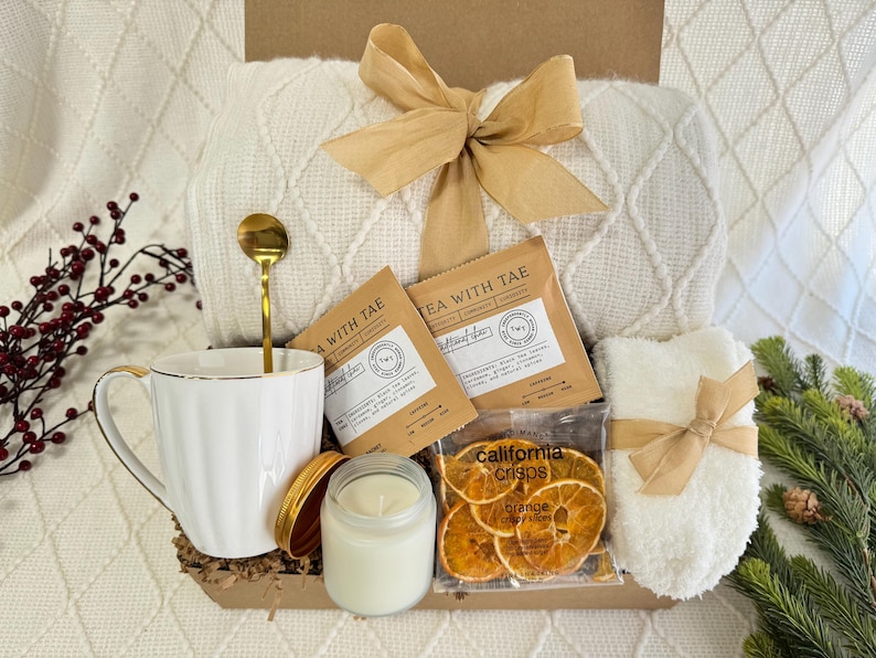 Peut inclure: Un panier-cadeau rempli d'articles confortables pour une soir&eacute;e relaxante. Il comprend une couverture en tricot blanc, une tasse blanche, une cuill&egrave;re dor&eacute;e, une bougie, une bo&icirc;te de chips d'orange et deux sachets de th&eacute; &eacute;tiquet&eacute;s "Tea with Tae".