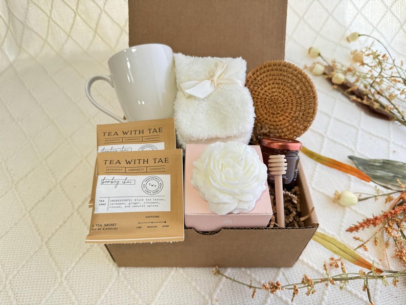 Peut inclure: Une bo&icirc;te-cadeau en carton marron remplie d'une tasse blanche, une serviette blanche, une fleur blanche, des sachets de th&eacute;, un pot de miel, un b&acirc;tonnet de miel en bois et un dessous-de-verre tiss&eacute;.