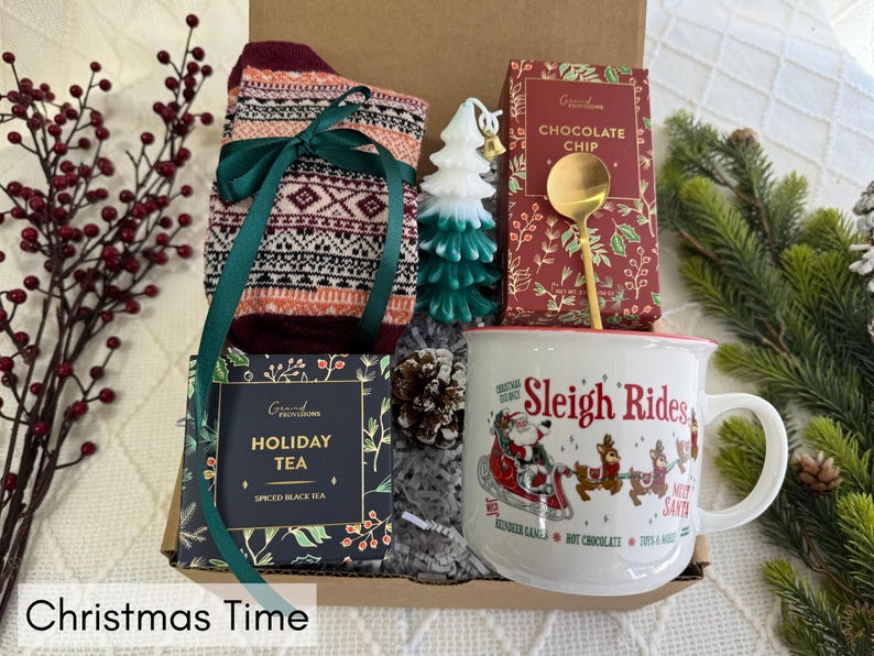 May include: A Christmas gift basket with a mug that says "Sleigh Rides", a box of holiday tea, a pair of patterned socks, a small tree ornament, and a box of chocolate chips.