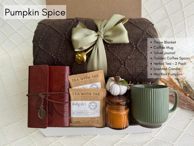 May include: A brown knitted throw blanket with a green satin ribbon, a brown leather journal, two tea bags, a green ceramic mug, a candle in a glass jar, and a small white knitted pumpkin. The text "TEA WITH TAE" is printed on the tea bags. The text "Pumpkin Spice" is printed at the top of the image.