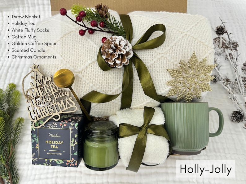 Christmas Holly Jolly gift box with white throw blanket, green mug, fluffy socks, holiday tea, gold spoon, scented candle, and Christmas ornaments arranged in cozy winter setting