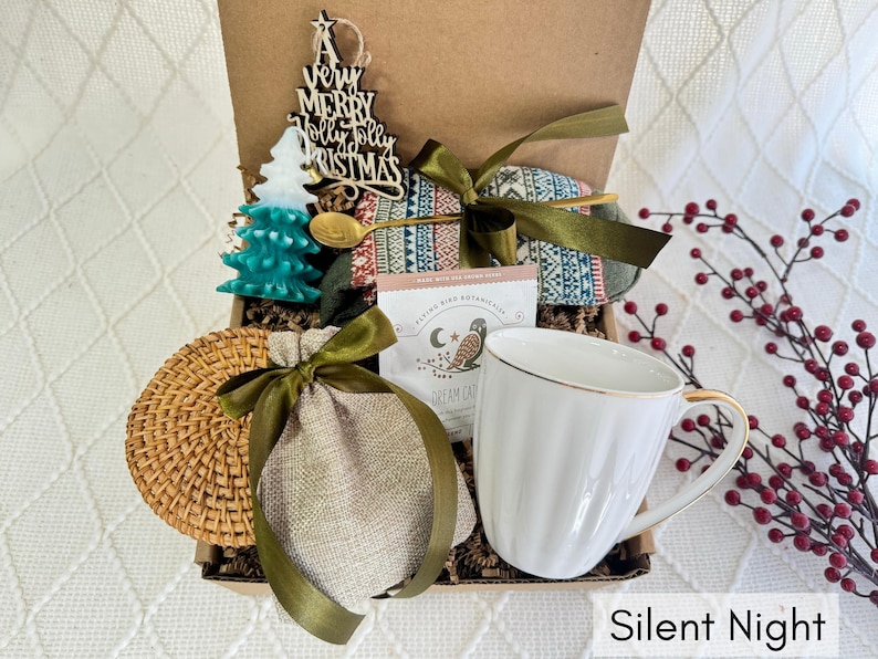 May include: A gift box filled with items for a cozy night in, including a mug, a bag of tea, a wooden ornament, and a woven coaster. The box is decorated with a green and red plaid fabric and the text "Silent Night".