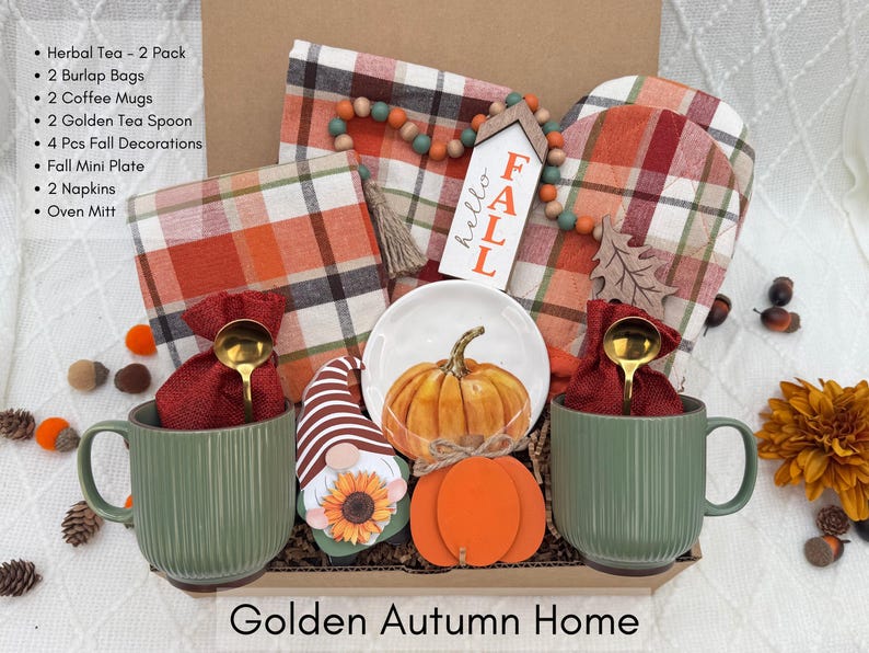 K&ouml;nnte beinhalten: Ein herbstliches Geschenkset mit zwei gr&uuml;nen Kaffeetassen, einem kleinen wei&szlig;en Teller mit einem K&uuml;rbis und herbstlichen Dekorationen. Enth&auml;lt einen Mini-Teller, Servietten und einen Ofenhandschuh. Der Text "Golden Autumn Home" steht unten.