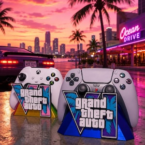 Puede incluir: Dos mandos de videojuegos blancos sobre soportes con el logotipo de Grand Theft Auto VI y gráficos de palmeras. Los mandos están colocados frente a un vibrante atardecer con el horizonte de una ciudad, un coche morado y un letrero de neón Ocean Drive.