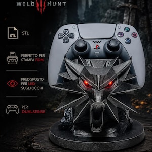 Può includere: Un controller DualSense grigio appoggiato su un supporto nero stampato in 3D a forma di medaglione del lupo di The Witcher. Il supporto ha una finitura metallica e occhi rossi luminosi. Il testo "THE WITCHER WILD HUNT" appare in alto.