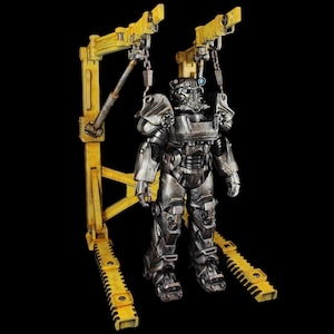 May include: A silver and black power armor figure is suspended from a yellow metal crane. The figure is standing upright with its arms at its sides. The crane has two yellow metal arms that are extended out to the sides. The figure is on a black background.