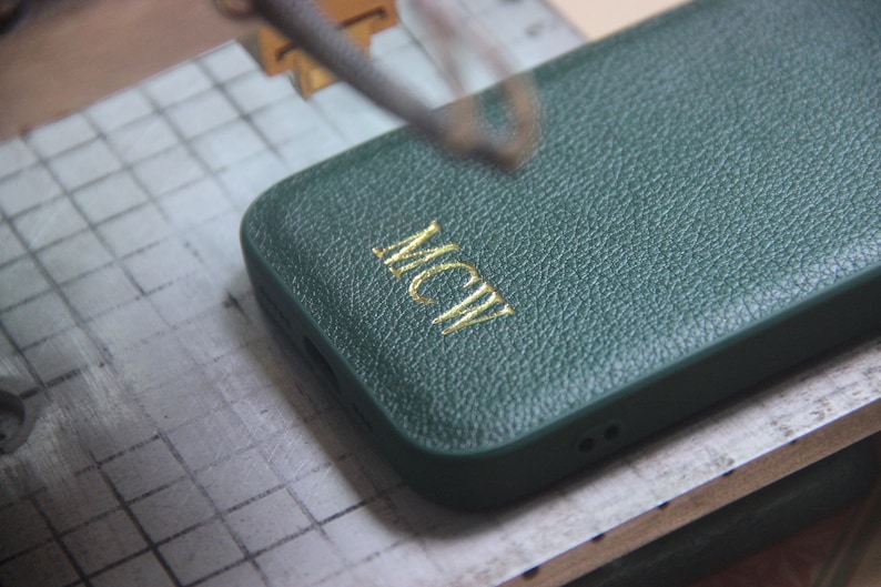 May include: A green leather phone case with gold lettering that says "MCW".