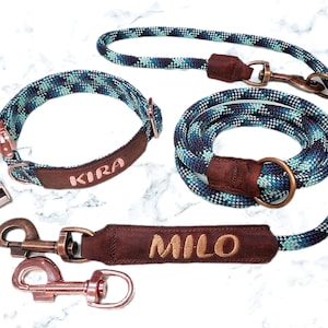 Könnte beinhalten: Ein blaues und grünes Hundehalsband und eine Leine aus Seil mit braunen Lederakzenten. Das Halsband ist mit dem Namen "KIRA" personalisiert und die Leine mit dem Namen "MILO".