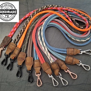 May include: A collection of colorful rope leashes with leather accents and metal clasps. The leashes feature various patterns and colors, including pink, orange, blue, and green. The image includes a logo that says "HANDMADE".
