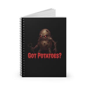 Puede incluir: Cuaderno de espiral con una cubierta negra. Presenta un monstruo de patata de dibujos animados con ojos rojos brillantes y el texto "GOT POTATOES?" en letras rojas goteantes. El cuaderno tiene páginas rayadas blancas.