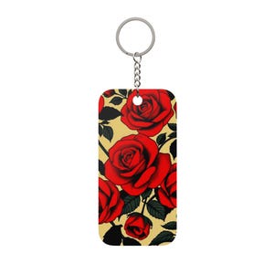 May include: A rectangular keyring with a pattern of red roses on a yellow background. The roses have detailed petals and are surrounded by dark green leaves. The keyring has a silver-coloured ring and chain.