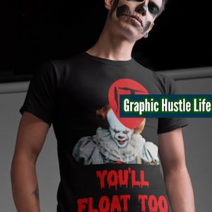 Könnte beinhalten: Schwarzes T-Shirt mit einem Grafikdruck von Pennywise dem Clown aus dem Film "Es" und dem Text "You'll Float Too". Die Grafik ist in Rot und Weiß. Der Text ist in Rot mit tropfenden Bluteffekten. Das T-Shirt hat einen roten Kreis mit einem Grafikdruck des Buchstabens "T" in der oberen rechten Ecke. Der Text "Graphic Hustle Life" ist in Grün und Weiß.