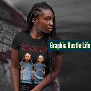 Peut inclure: T-shirt noir avec un imprimé graphique de deux filles en robes bleues. Le texte "REDRUM" est écrit en rouge au-dessus des filles.