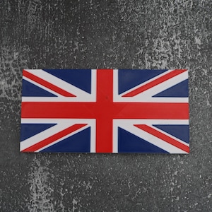 以下が含まれることがあります： 赤十字と白い斜めストライプが青い背景にある長方形のユニオンジャック旗。旗は、テクスチャ加工された濃い灰色の表面に配置されています。