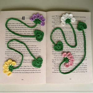May include: A crocheted bookmark with a variety of flowers in yellow, pink, white, and purple. The bookmark is attached to a book with the text "48" visible on the page.