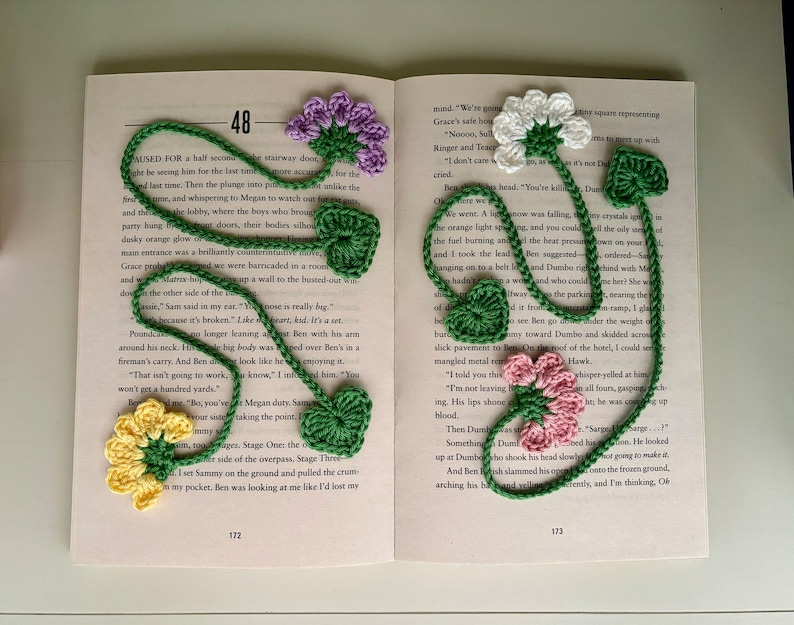 May include: A crocheted bookmark with a variety of flowers in yellow, pink, white, and purple. The bookmark is attached to a book with the text "48" visible on the page.