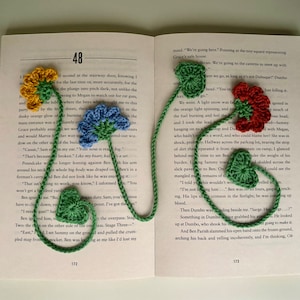 May include: A green, red, and blue crocheted bookmark with flower designs. The bookmark is hanging from a book with the text "48" and "172" visible.