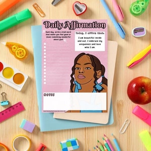 May include: A selection of stationery items, including a Daily Affirmation notepad with a portrait of a woman, pens, scissors, and pencils, arranged on a wooden surface. The notepad features the text "Daily Affirmation" and affirmations. Other items include a red apple and a pair of glasses.