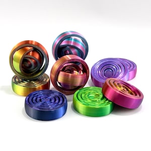 Può includere: Una collezione di fidget toy stampati in 3D con design sferici e circolari piatti. Gli oggetti presentano vivaci transizioni di colore sfumate, tra cui blu, verde, viola, arancione e rosa, con motivi a cerchi concentrici sulle superfici.