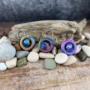Puede incluir: Tres llaveros de metal iridiscente con un diseño en espiral. Cada llavero tiene una combinación de colores diferente de azul, morado, verde y dorado.