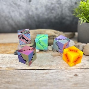 Può includere: Cinque cubi geometrici stampati in 3D di colori vivaci con disegni intricati. I cubi sono realizzati in un materiale liscio e lucido e presentano una varietà di colori, tra cui viola, verde, blu, arancione e un motivo a strisce multicolore.