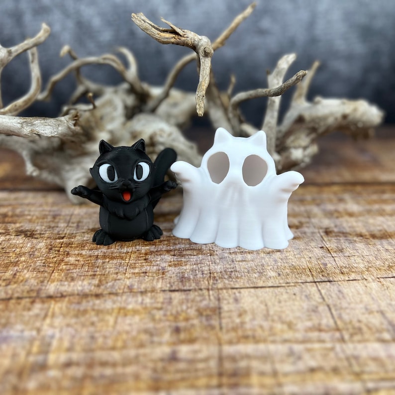 May include: A black cat figurine with white eyes and a red mouth, standing next to a white ghost figurine with two holes for eyes.