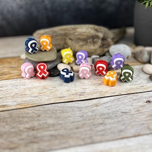 Può includere: Assortimento di ciondoli in silicone colorati a forma di nastri di consapevolezza. I ciondoli sono di vari colori, tra cui rosso, rosa, blu, giallo, arancione, viola e verde.