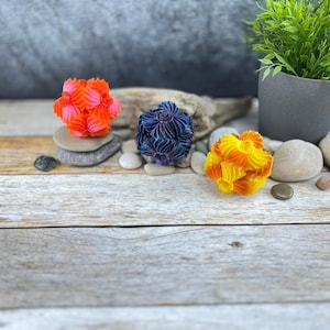 Può includere: Tre sfere di origami colorate, una arancione, una blu e una gialla, sono disposte su una superficie di legno con pietre.