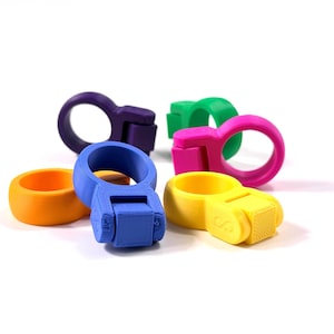 Könnte beinhalten: Eine Sammlung von sechs 3D-gedruckten Kunststoffhaltern in Ringform in leuchtenden Farben wie Violett, Grün, Pink, Gelb, Orange und Blau. Jeder Halter besteht aus einem kreisförmigen Band, das an einem kleinen, quadratischen Block mit Textur befestigt ist.